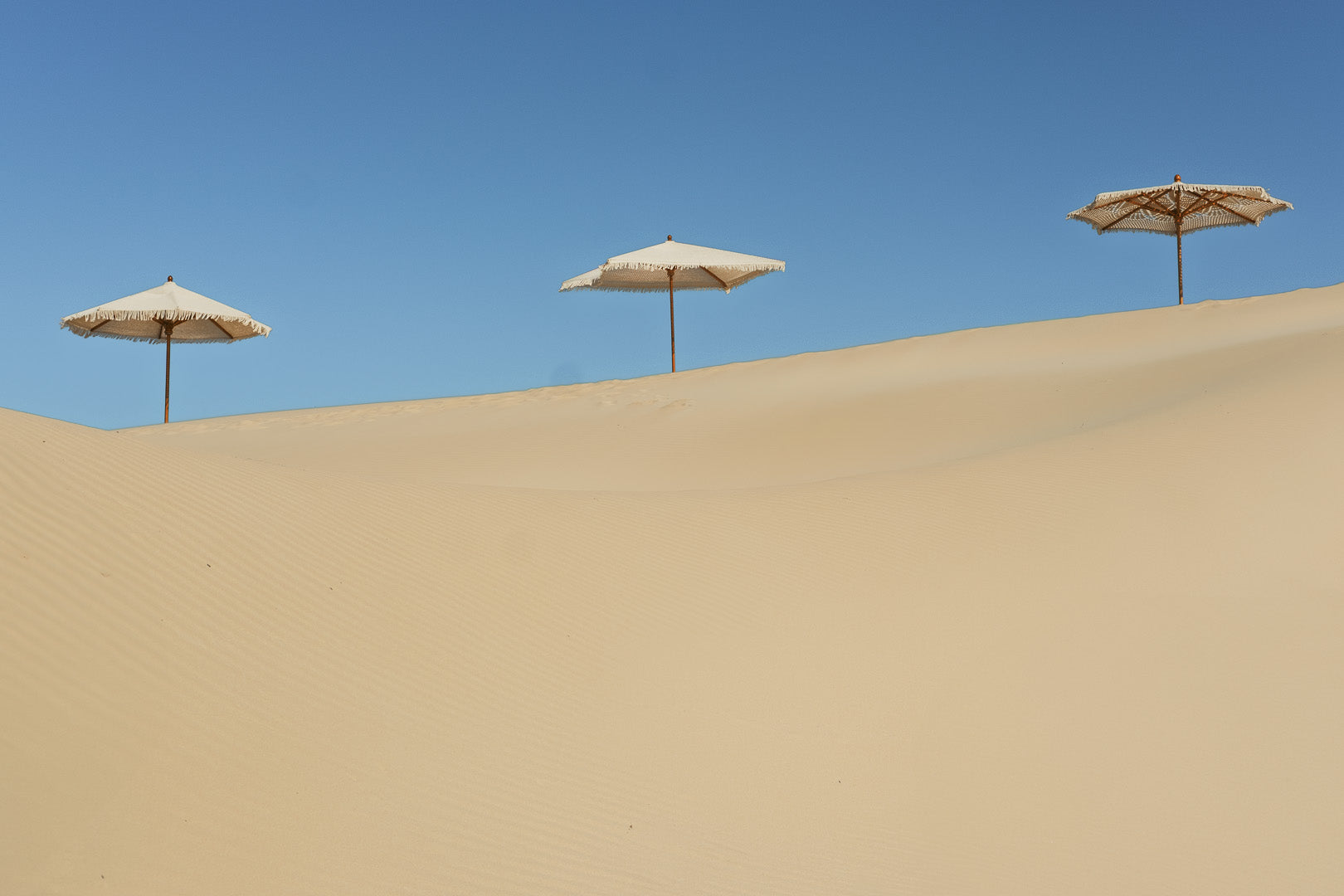 three handcrochet parasols lines up on a sand dune with clear blue sky